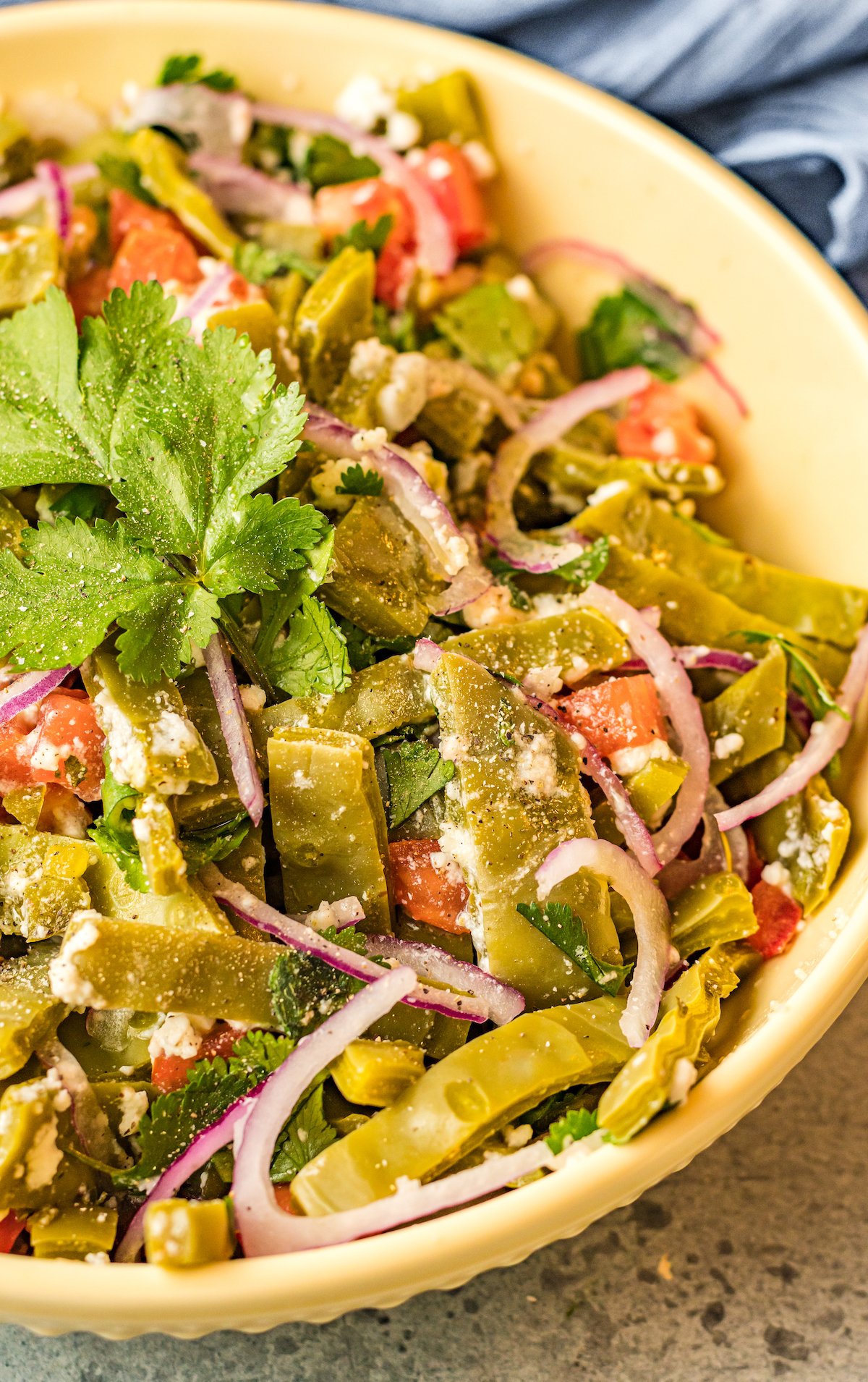 Prepared cactus salad topped with cilantro sits in a yellow serving bowl