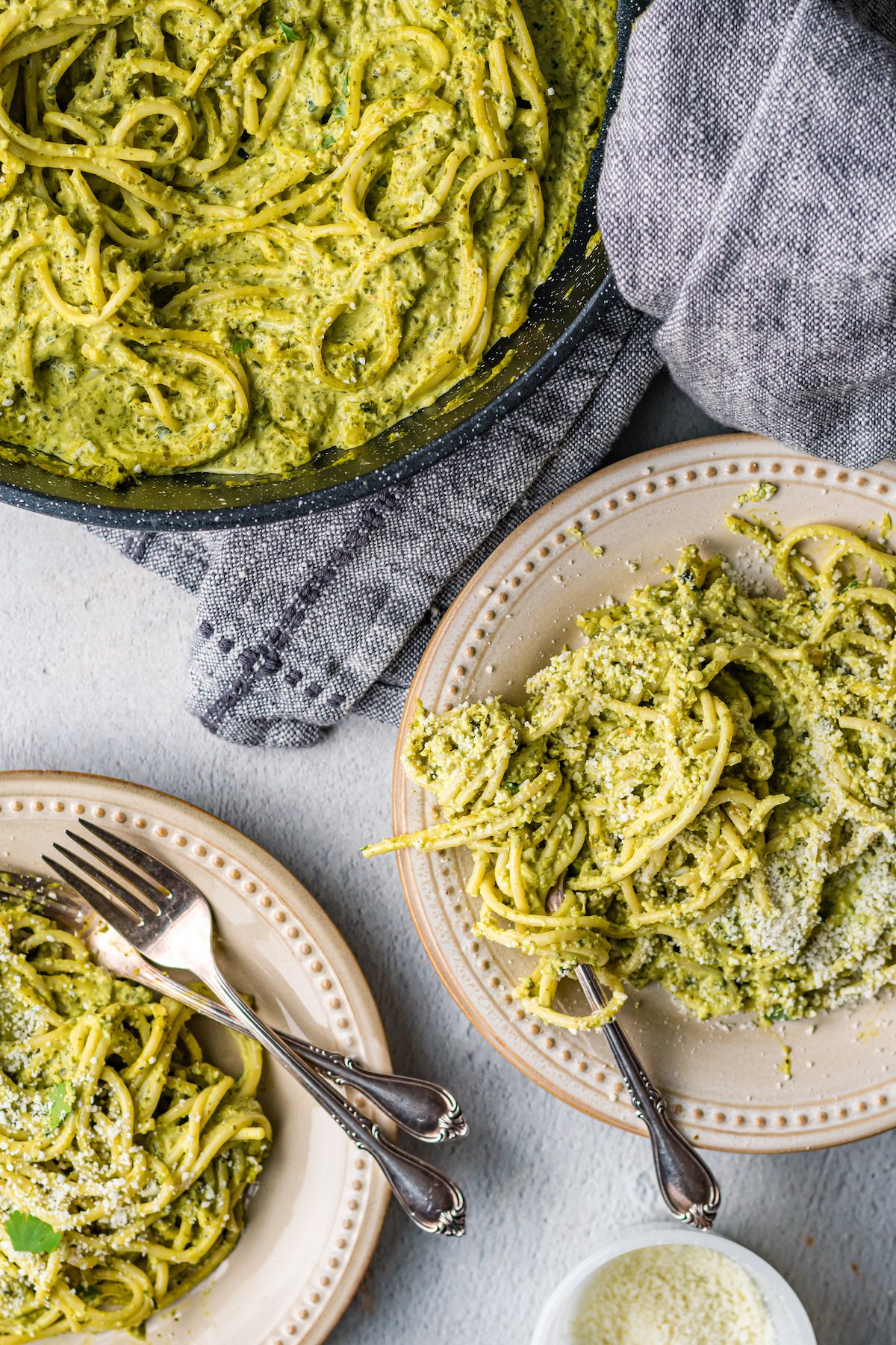 Overhead look at two dinner plates with green mexican spaghetti next to a pan full of it.