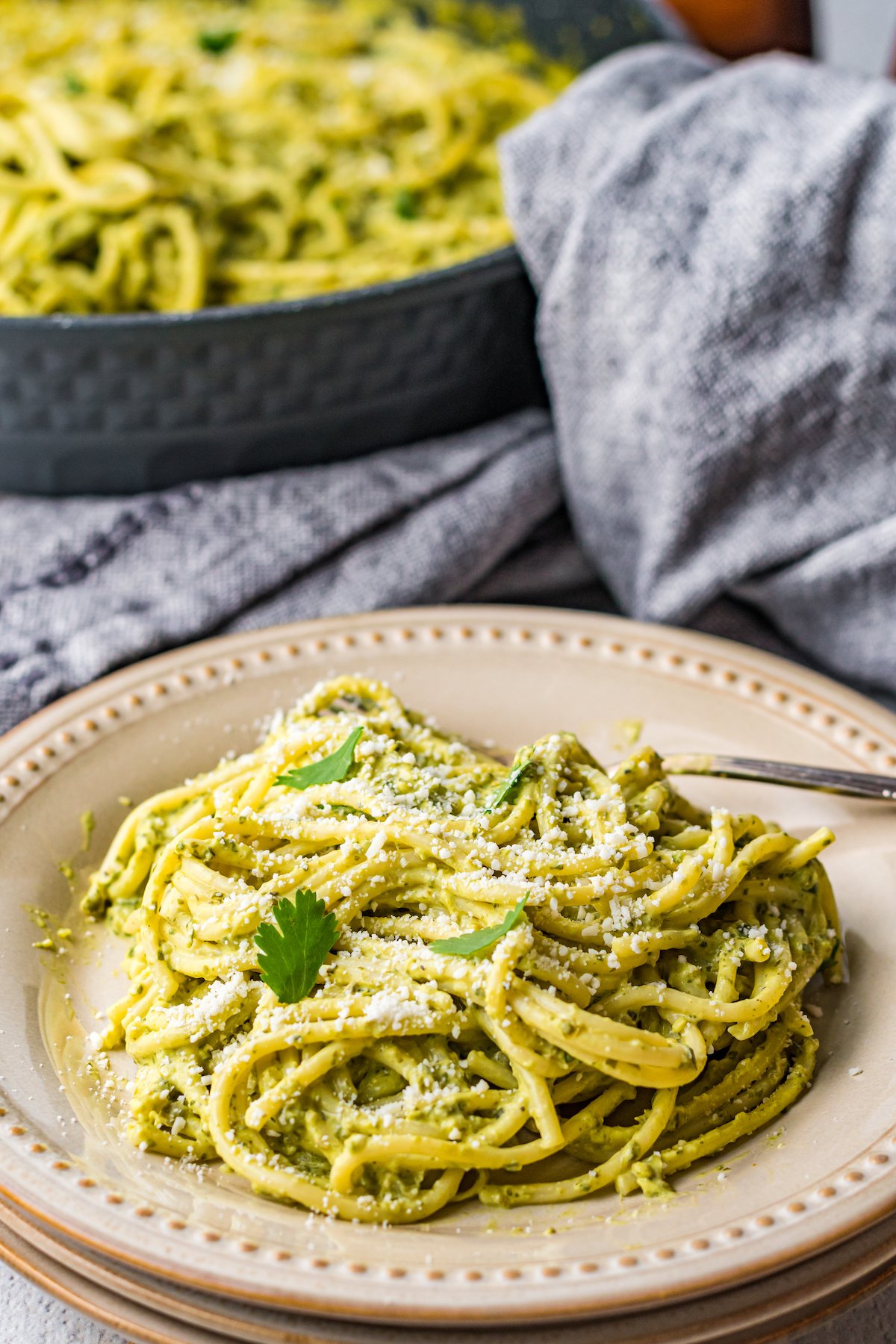 A dinner plate of green Mexican spaghetti sits in front of a pan filled with it as well