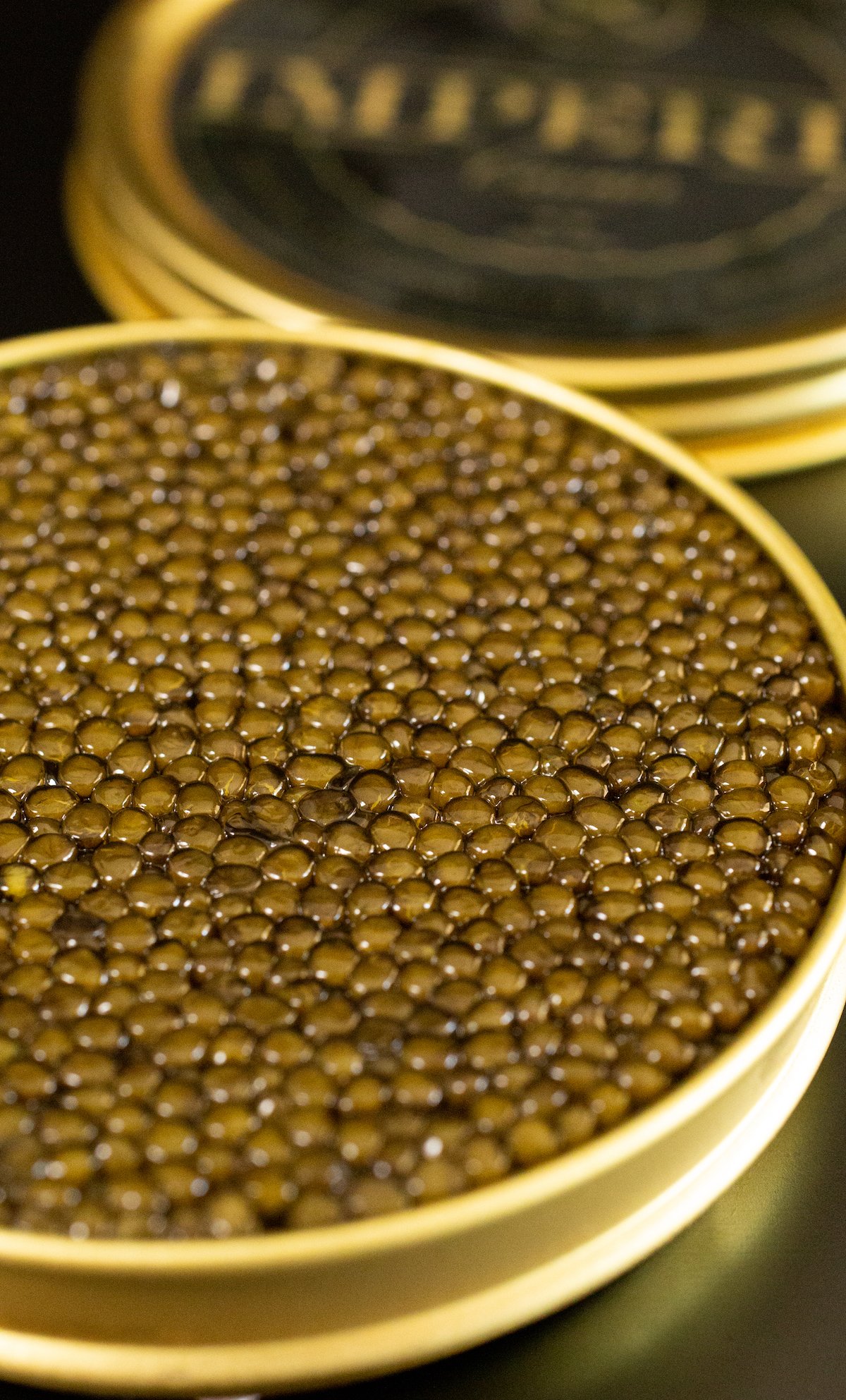 An open tin of golden osetra caviar sits on a black table
