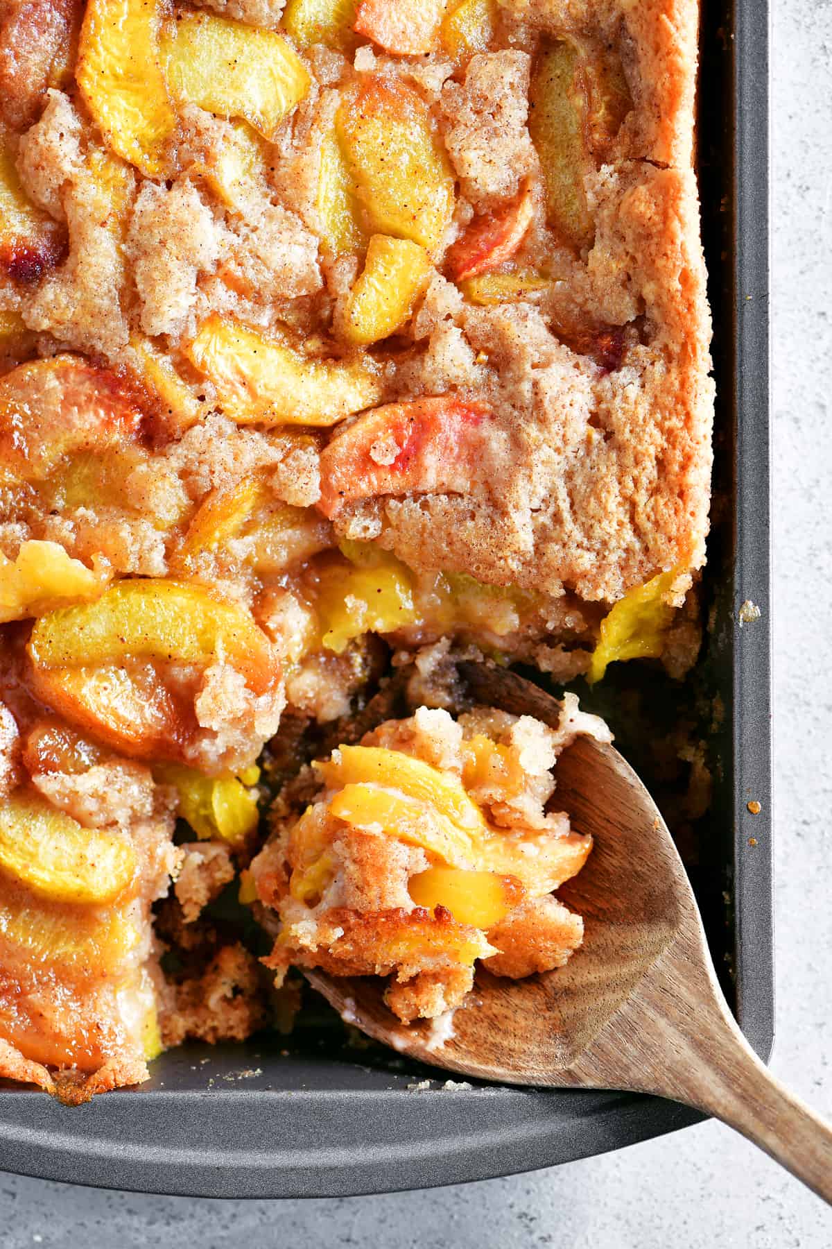 A pan of cooked peach cobbler made with Bisquick has a scoop taken out of it with a wooden spoon.