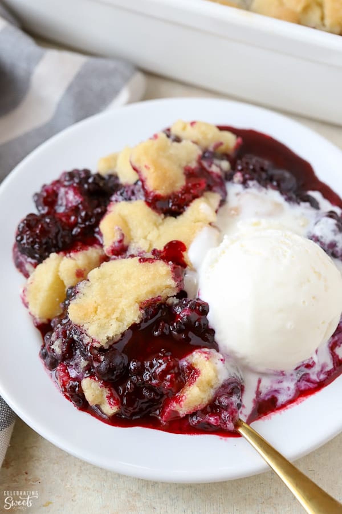 A bowl filled blackberry cobbler and a scoop of vanilla ice cream that has already started to melt.
