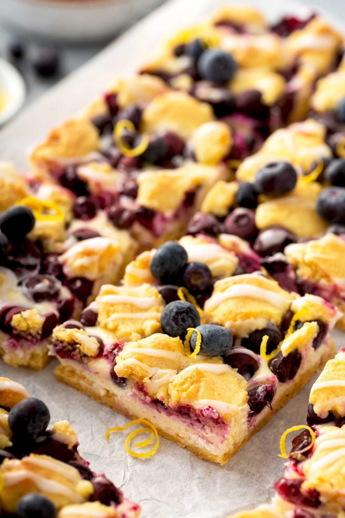 A pan of lemon blueberry cheese cake bars have been cut into squares.