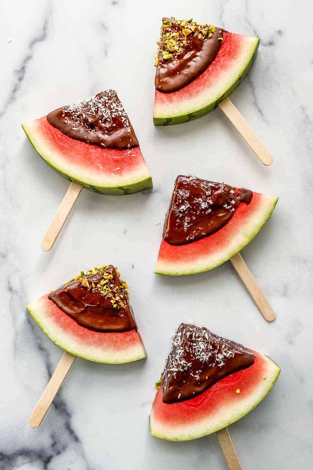 Overhead few of watermelon slices that have been dipped in chocolate and are on popsicle sticks.