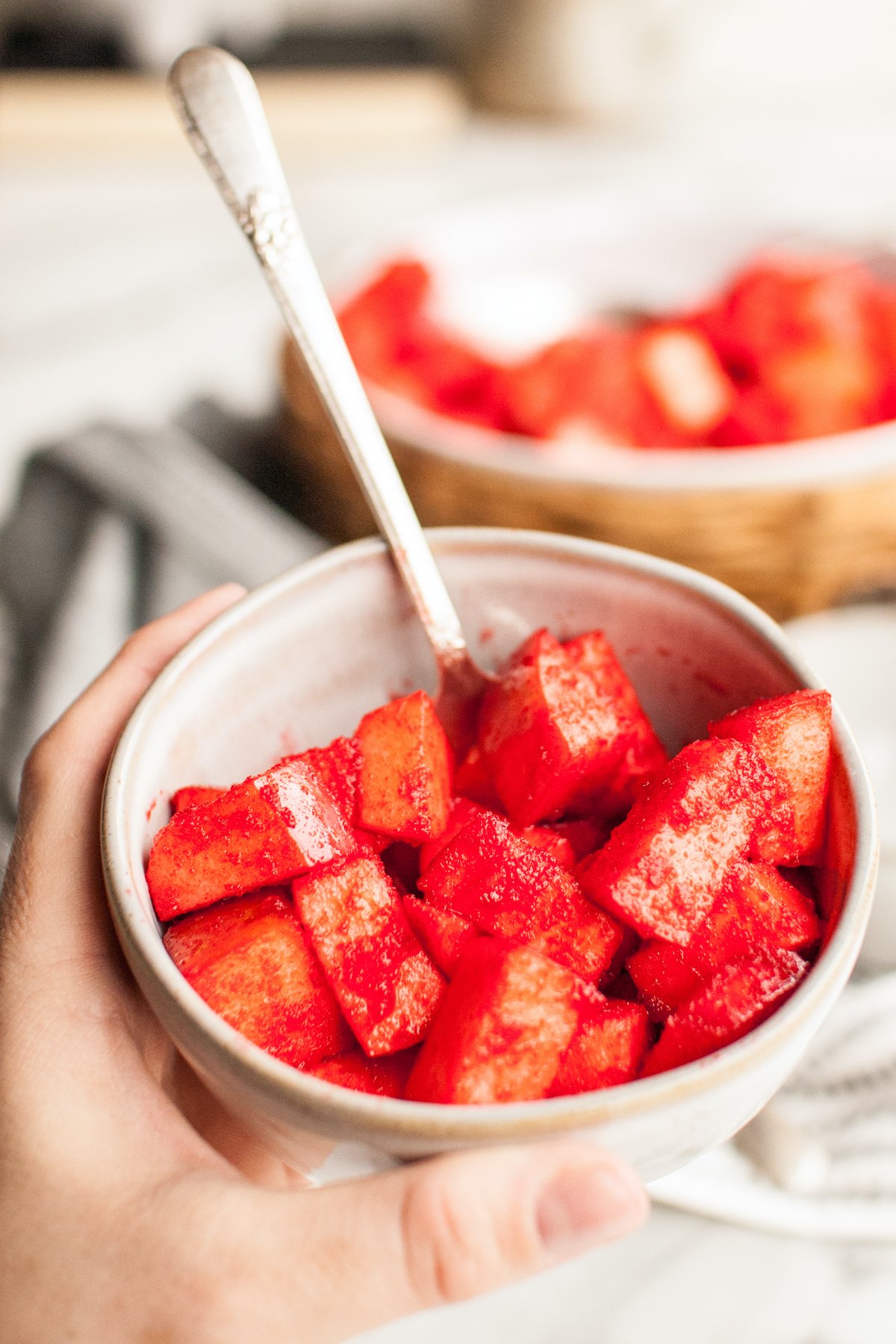 A hand holds a light colored bowl filled with chopped apples that have been covered in red jello.