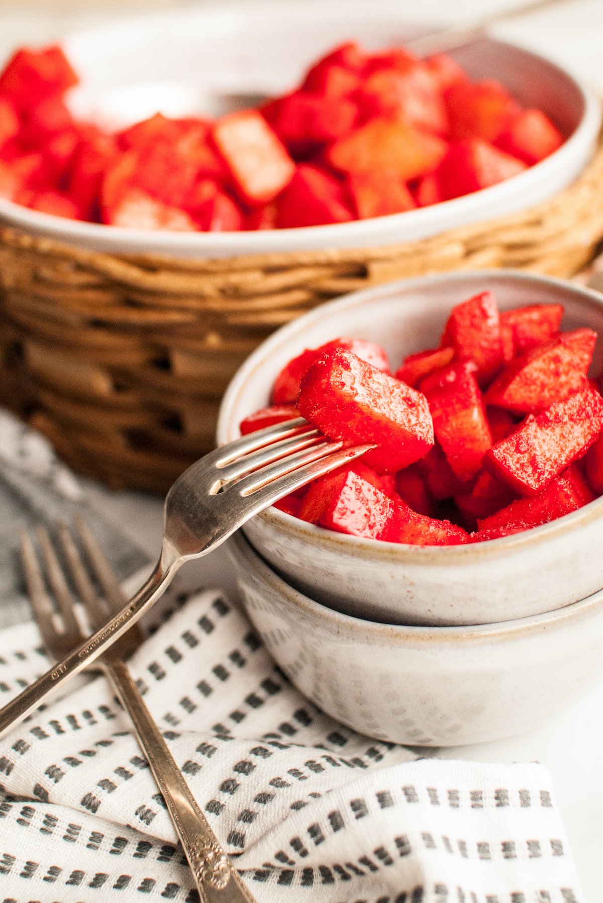 A fork holds a single apple piece from a bowl of cherry Jello covered apples