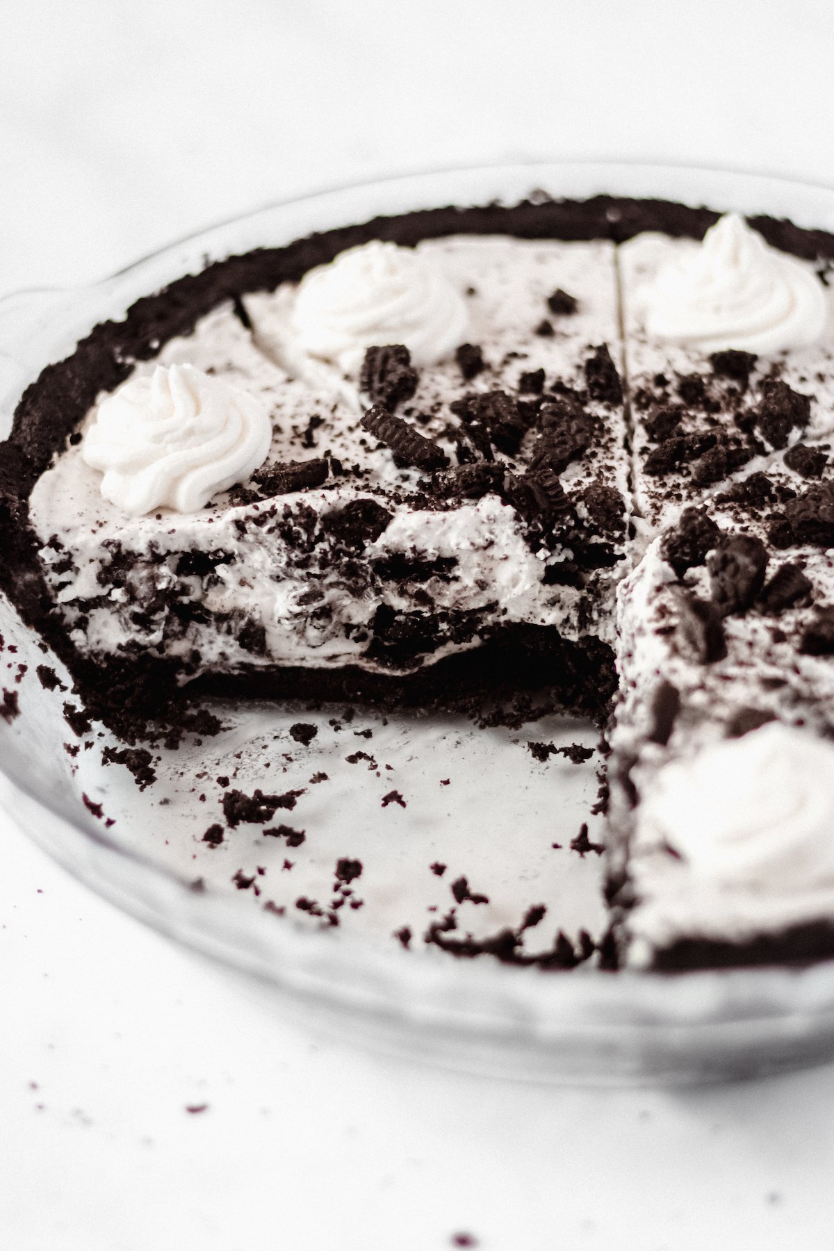 A cookies and cream pie in a glass pie dish on a white background. Two slices have been removed.