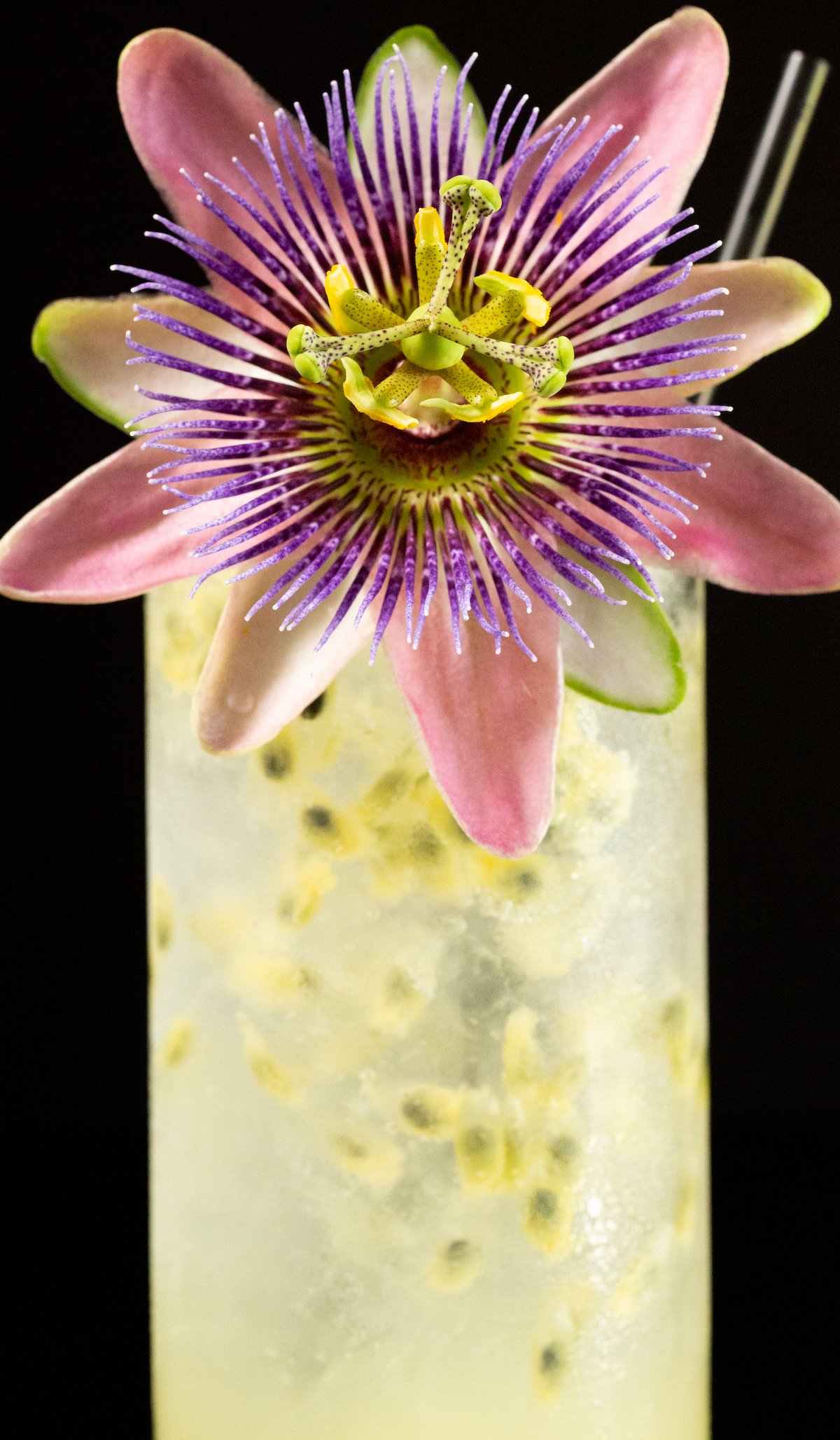 A cocktail with passion fruit puree is garnished with a passion fruit flower and black straw