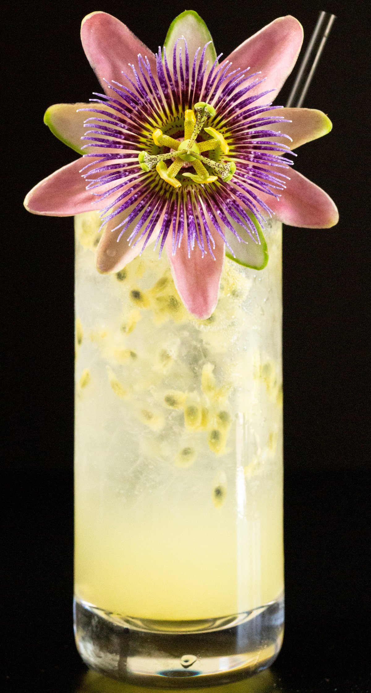 A passion fruit cocktail in a highball glass is garnished with a passion fruit flower