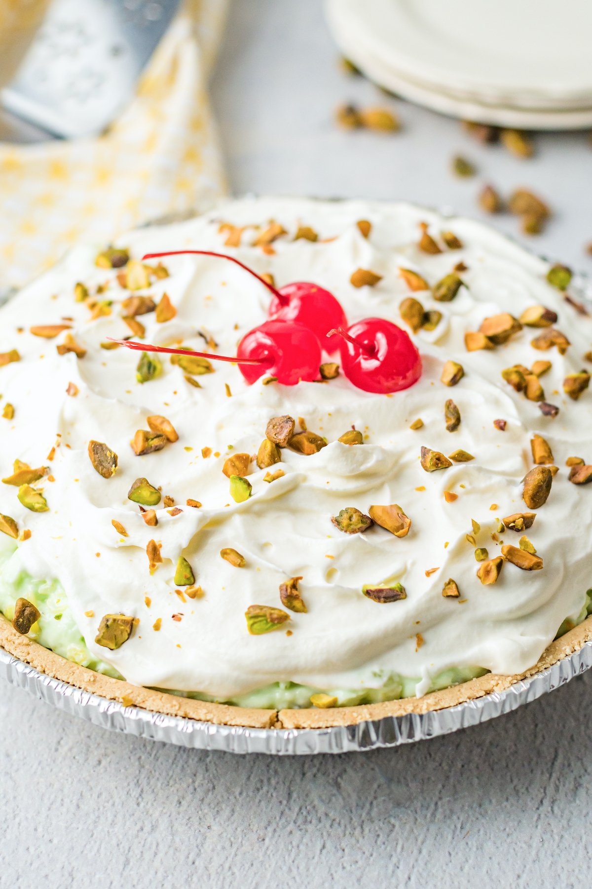 An uncut pistachio pie topped with whipped cream, chopped pistachios, and maraschino cherries.