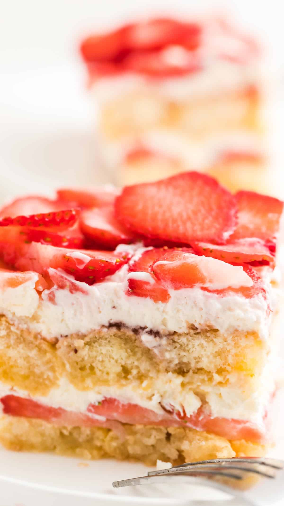 Close up of a cut piece of strawberry tiramisu showing the layers of lady fingers, strawberries, and whipped cream.