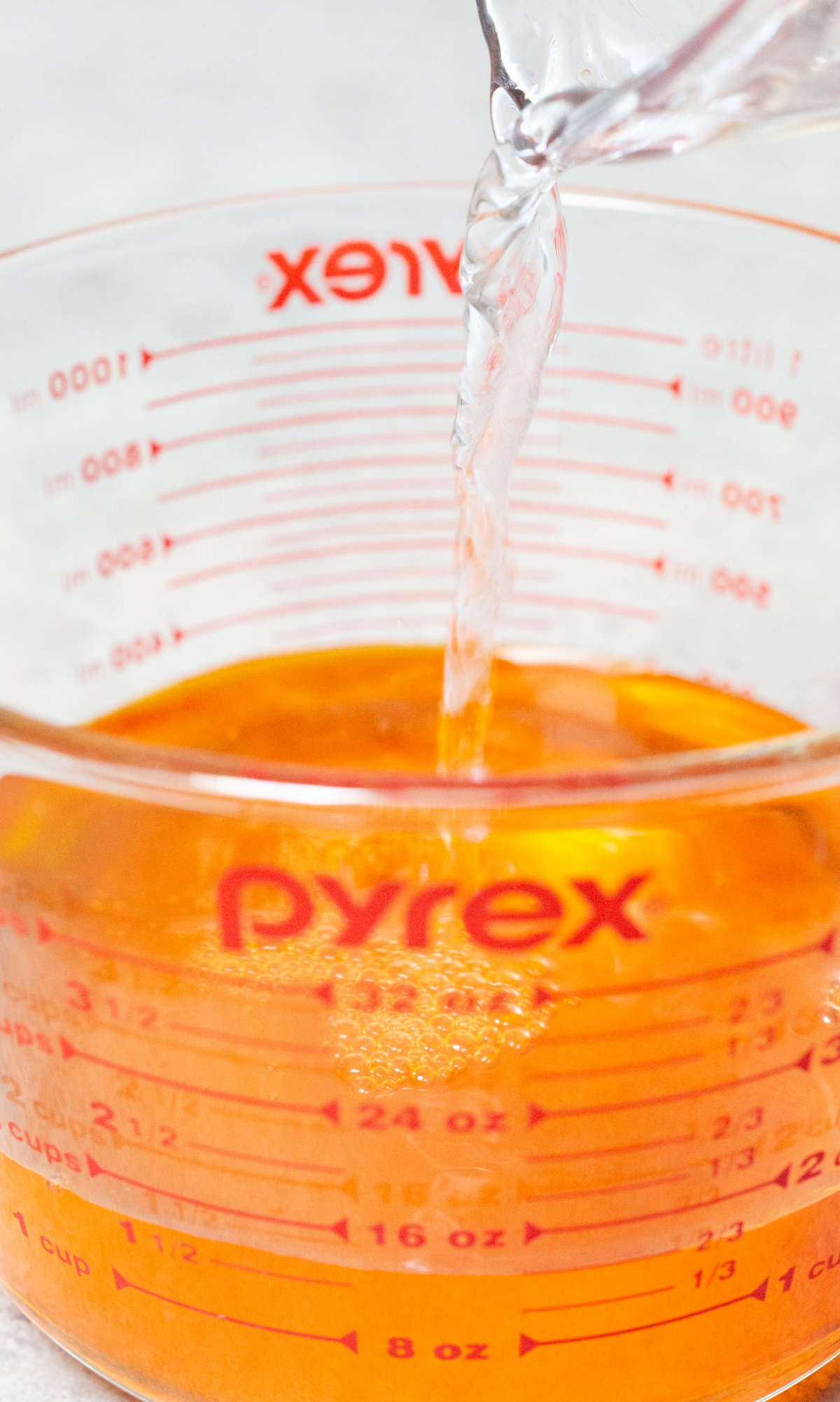 Water being poured into a large pyrex measuring cup that already has orange syrup in it.