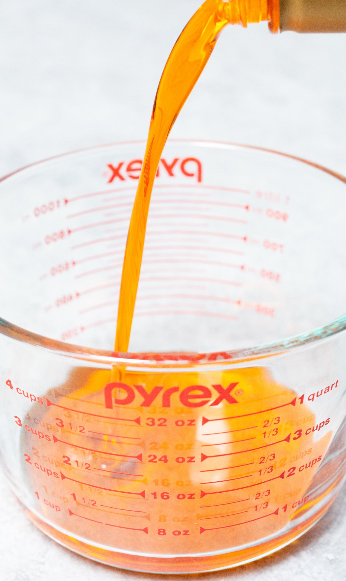 Orange syrup being poured into a large glass pyrex measuring cup.