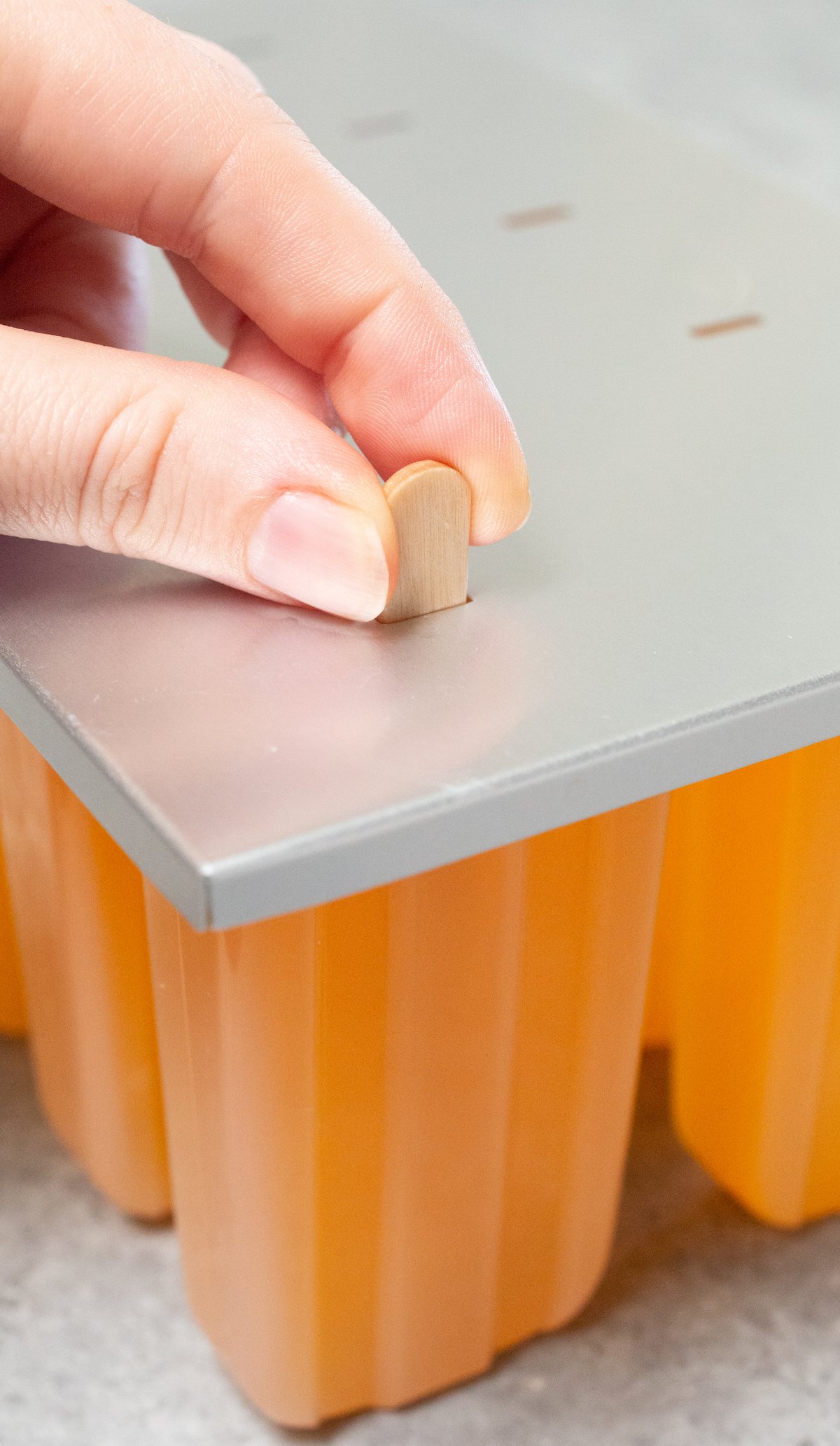 A hand inserts a stick into the top of a popsicle mold.