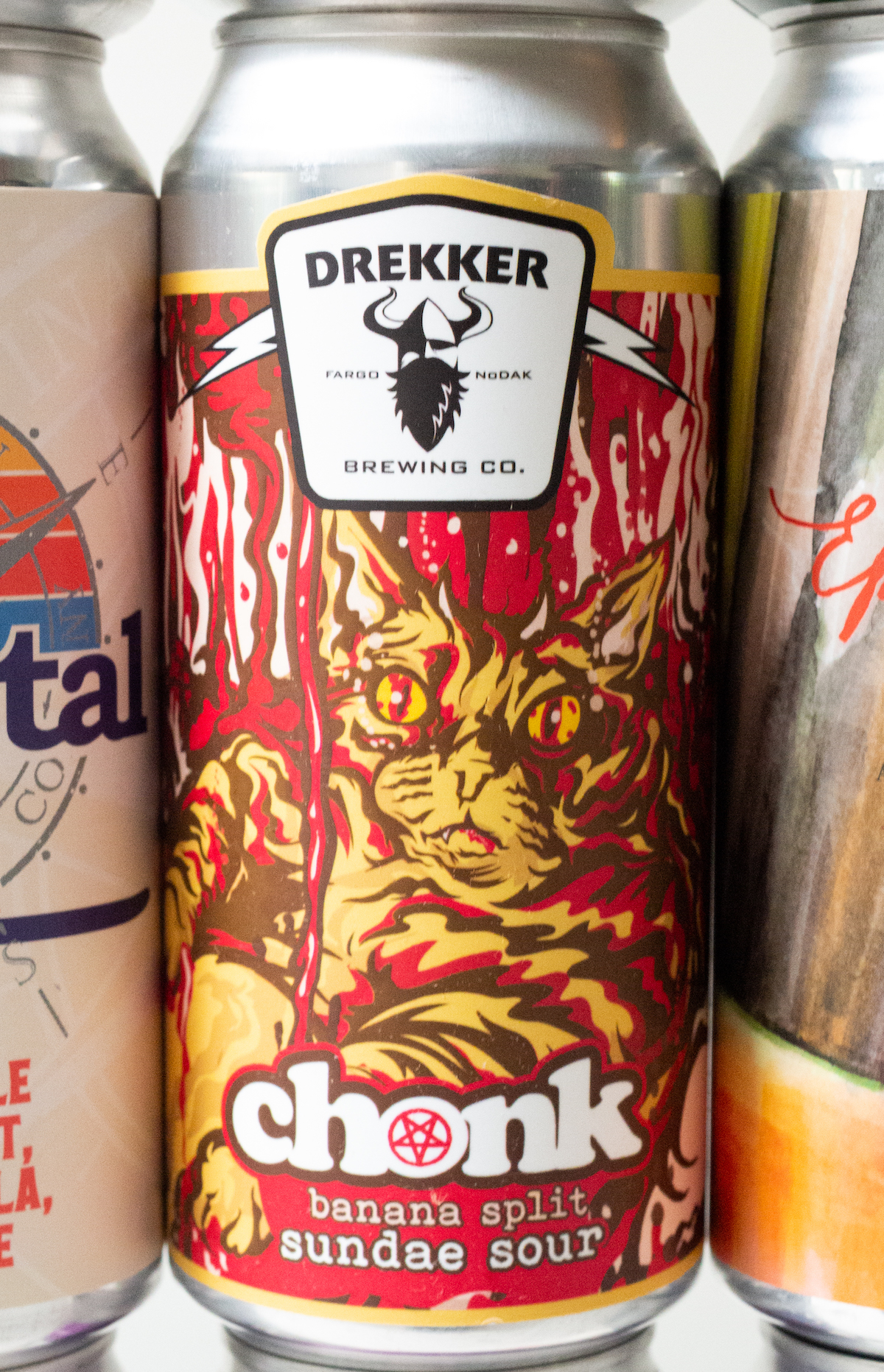 Close up of a can of "Chonk" by Drekker sour beer. The label is hues of red, yellow, and brown and features a drawing of a cat.