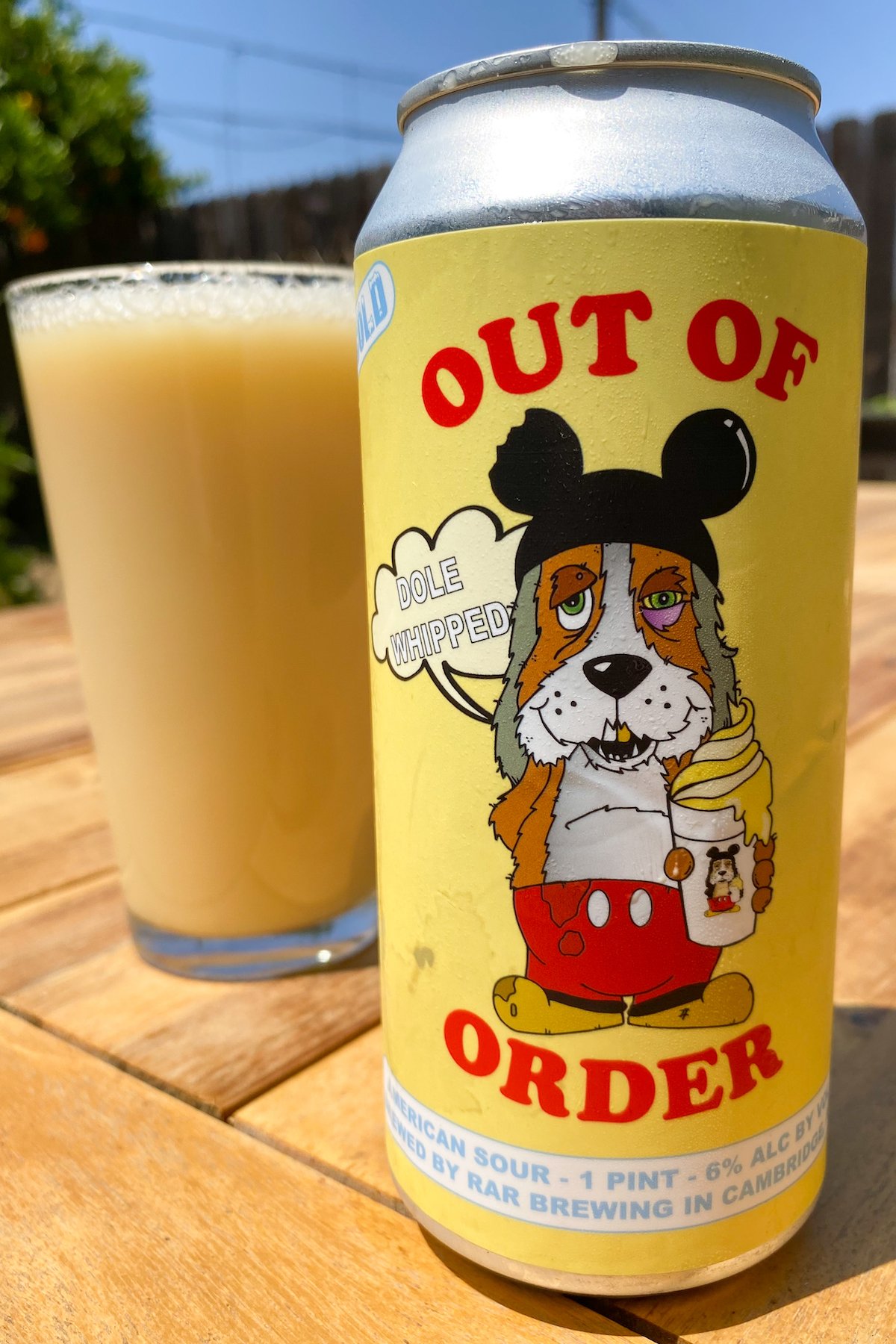 A yellow Out of Order beer can sits in front of a pint glass that the pineapple dole whip beer has been poured into.