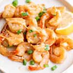 A white dinner plate filled with hibachi shrimp that's been drizzled with yum yum sauce.