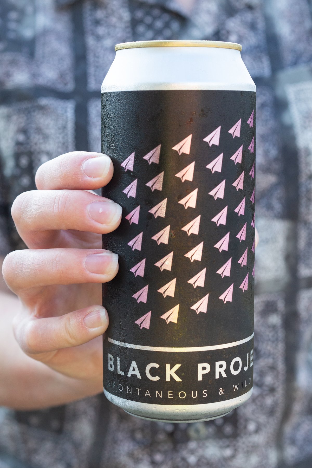 A hand holds a black beer can that reads "Black Project Wild & Spontaneous Ales"