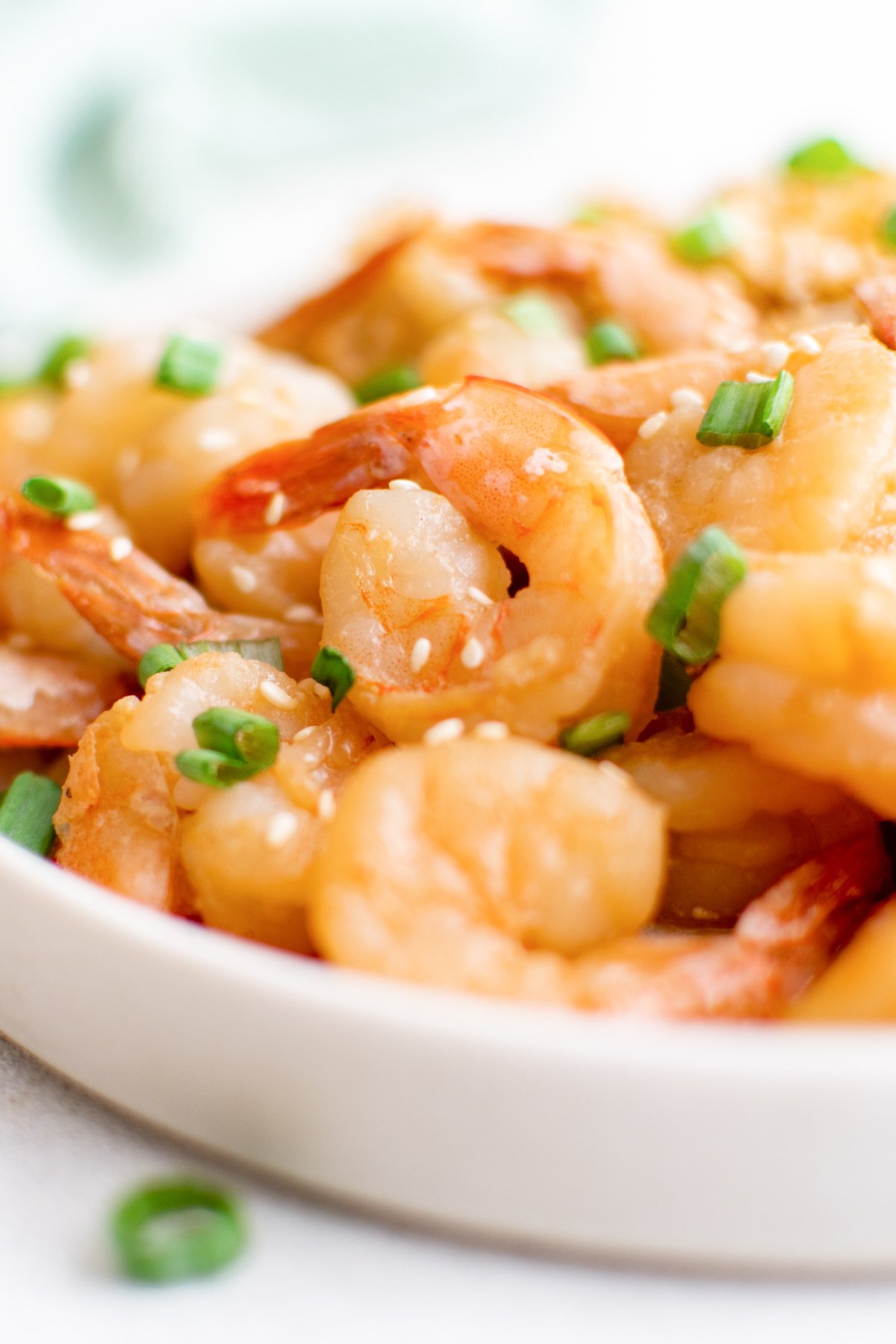 A white plate filled with cooked hibachi shrimp that's covered in sesame seeds and sliced green onions.