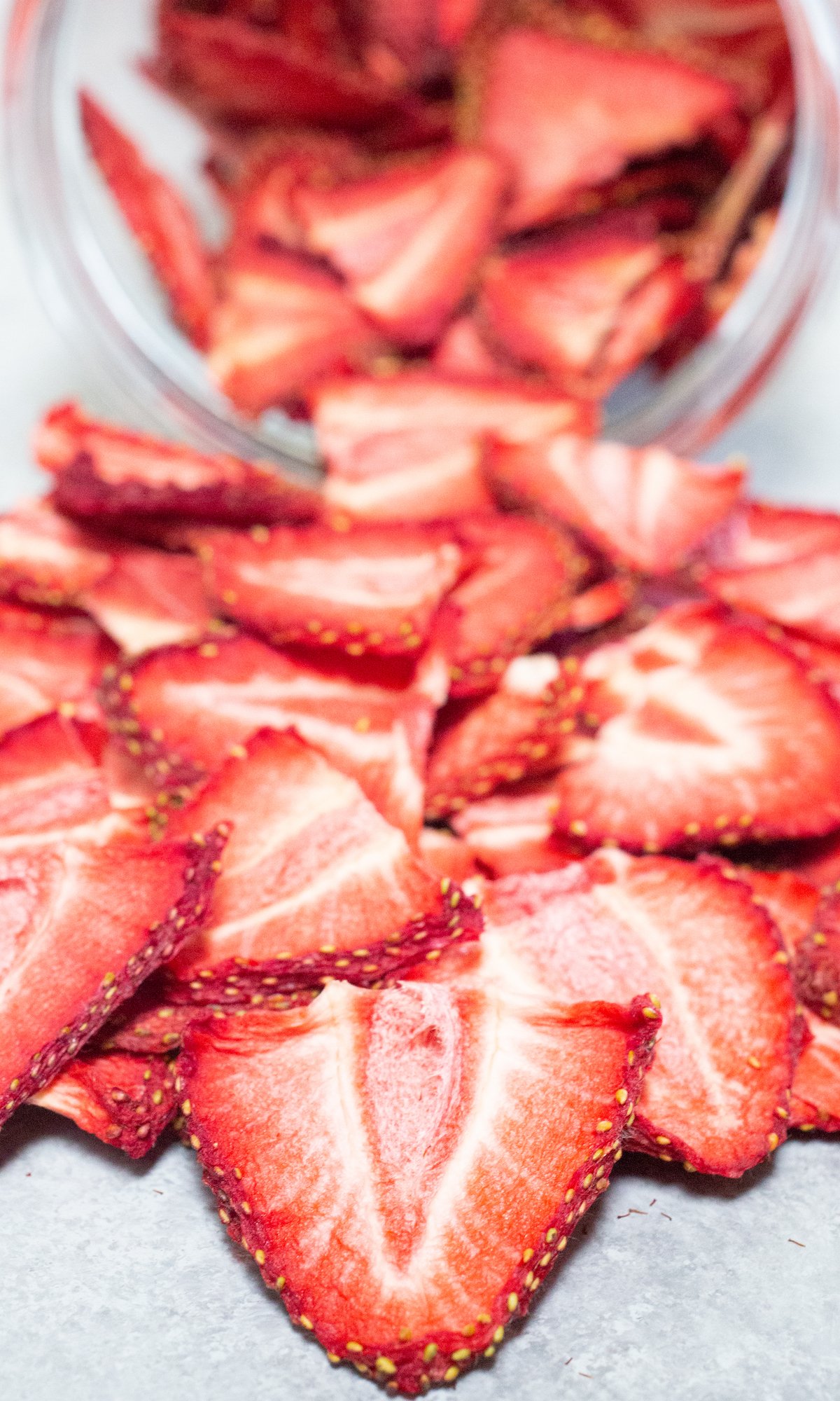 Dehydrated strawberry chips pouring out of a glass jar.