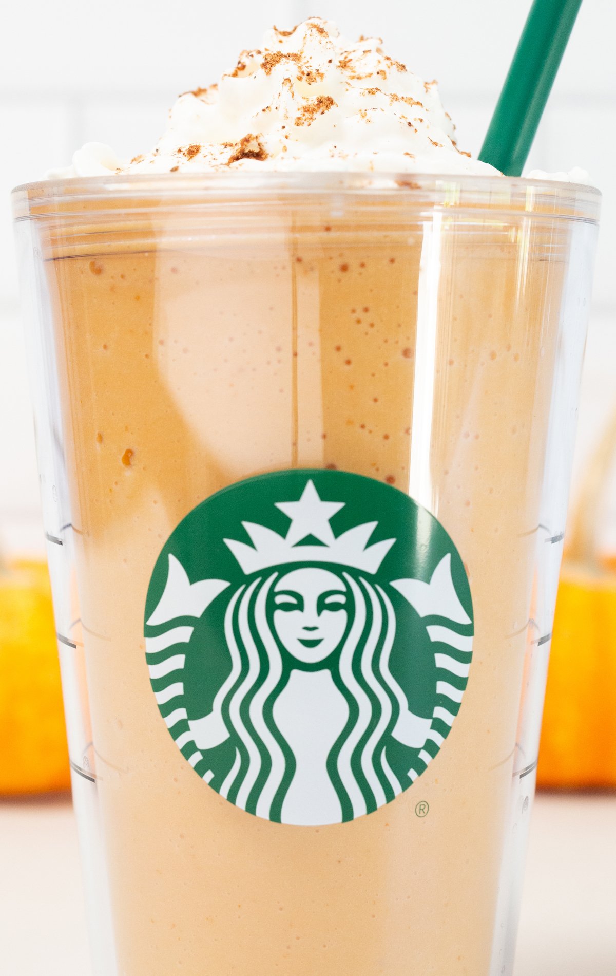 A large plastic tumbler glass with the Starbucks logo is filled with a pumpkin spice frappuccino that's been topped with whipped cream and pumpkin pie spice.