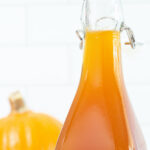 Close up of a bottle of pumpkin spice syrup on a white background next to a pumpkin
