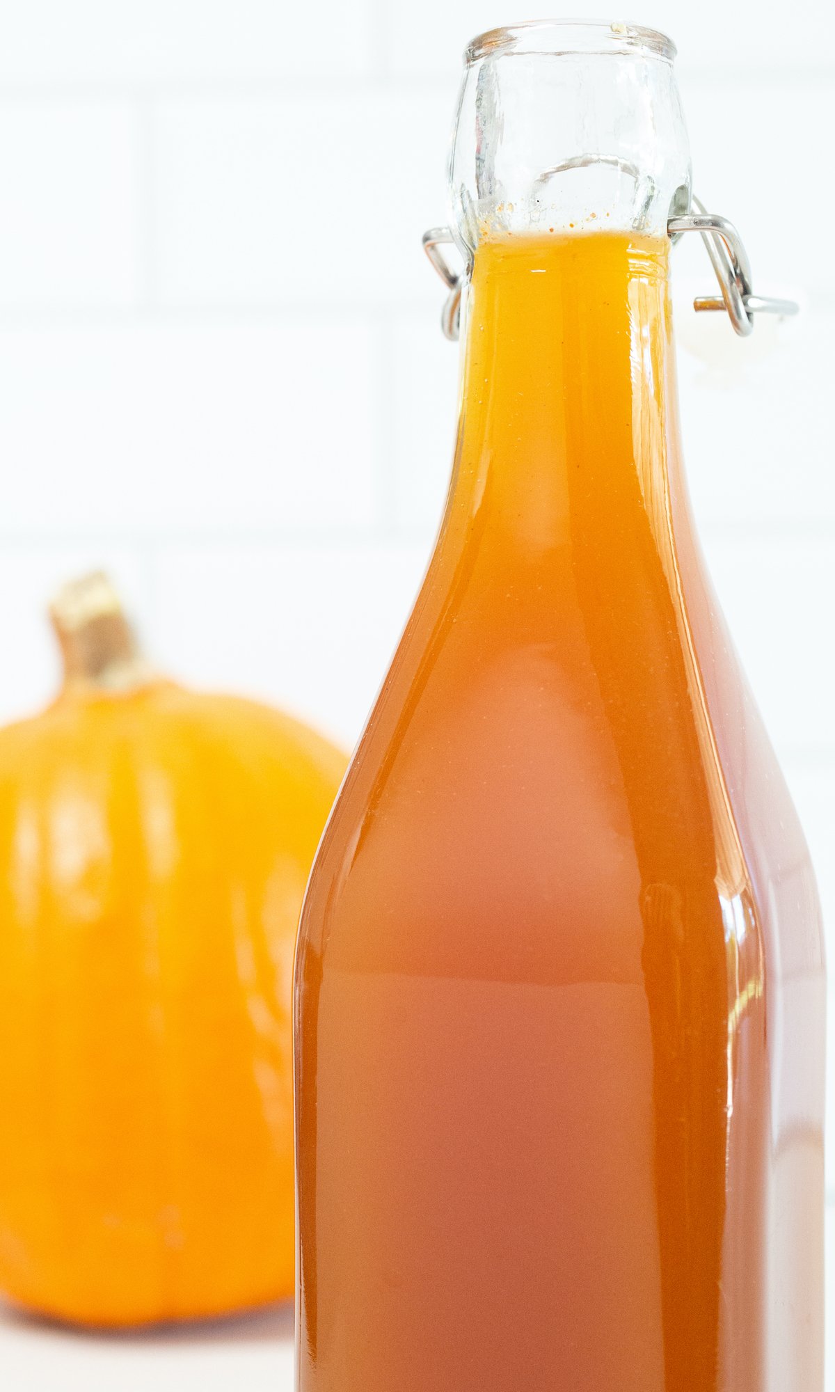 Close up of a bottle of pumpkin spice syrup on a white background next to a pumpkin