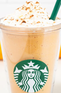 Close up of a starbucks plastic tumbler with a pumpkin spice frappucino and whipped cream on top.