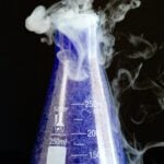 A purple sparkling witches brew served in a scientific flask cocktail with smoke coming out of the top.
