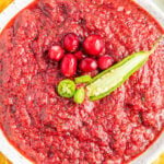 Overhead view of a white bowl filled with a pureed cranberry salsa that's garnished with whole cranberries and a sliced jalapeno pepper on top.
