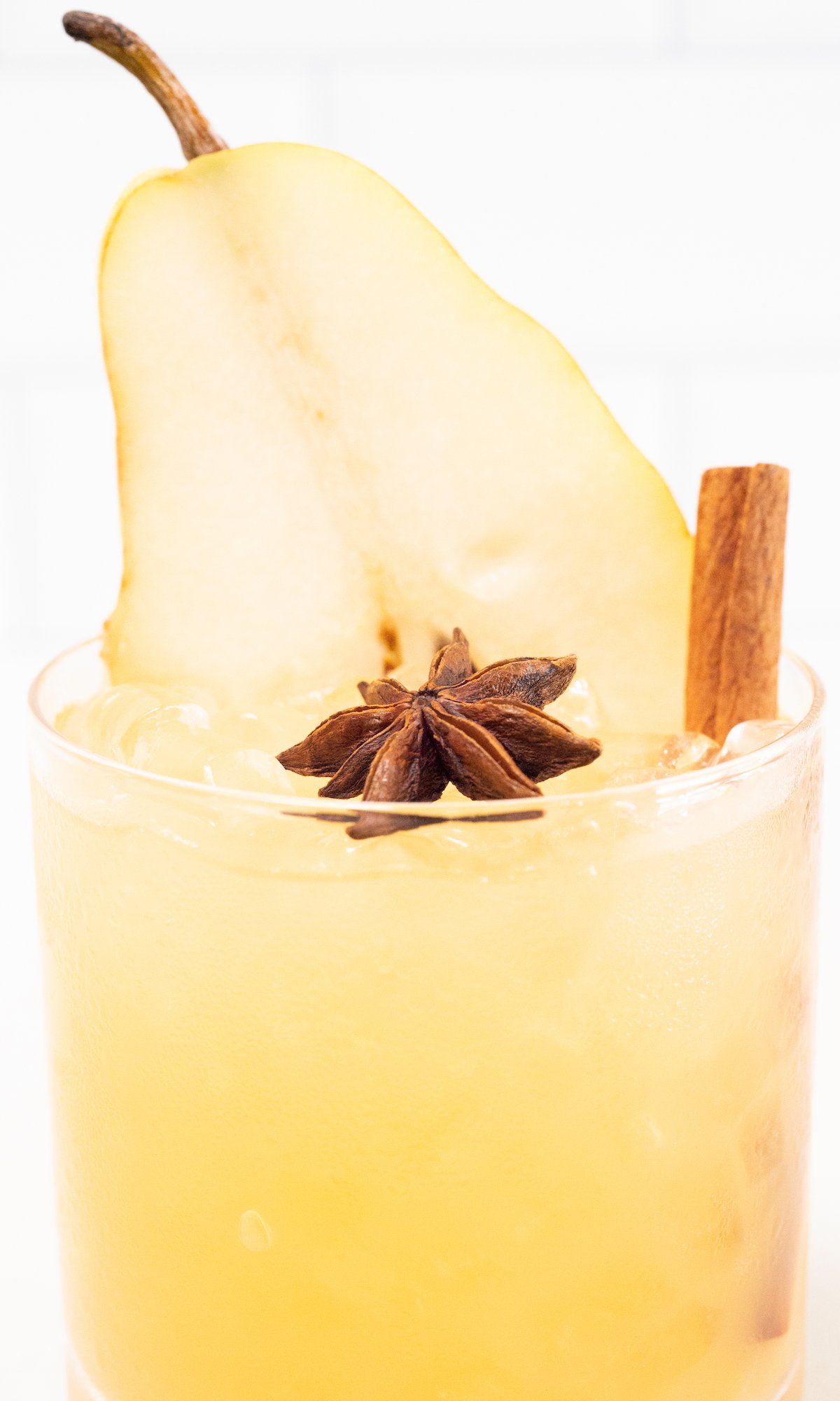 Close up of a Thanksgiving cocktail served in a lowball glass and garnished with a star anise, cinnamon stick, and pear slice.