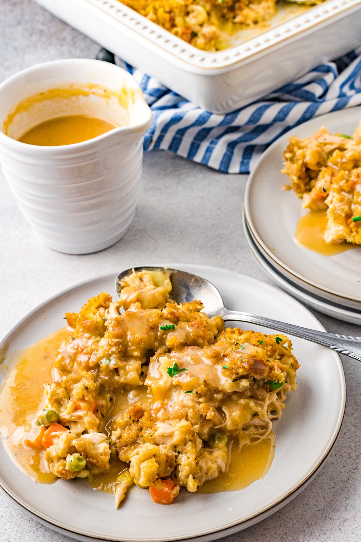 A white plate has a serving of turkey casserole on it. In the background you can see a container of gravy and the rest of the casserole in the baking dish.