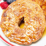 A sliced bagel that has been turned into french toast sits on a plate next to fresh berries.