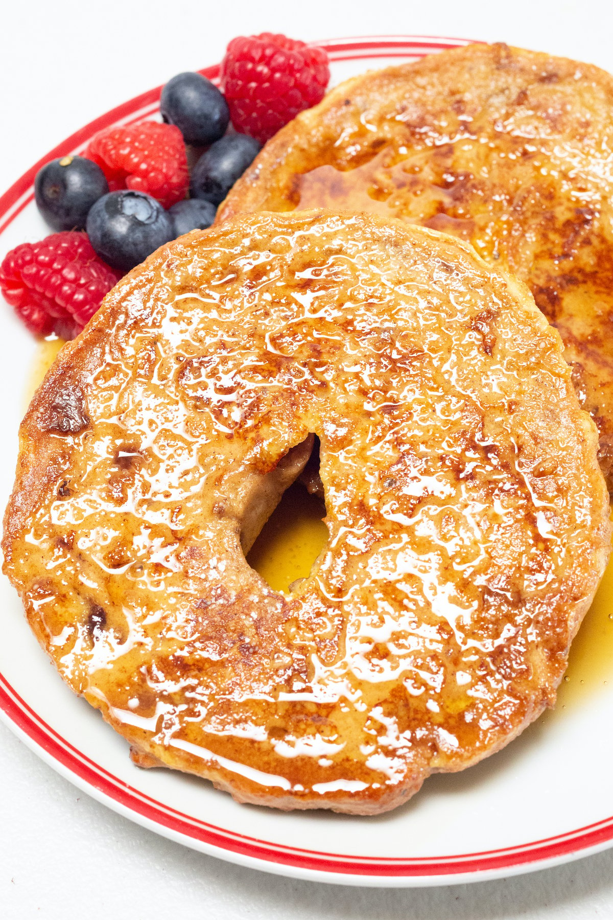 A sliced bagel that has been turned into french toast sits on a plate next to fresh berries.