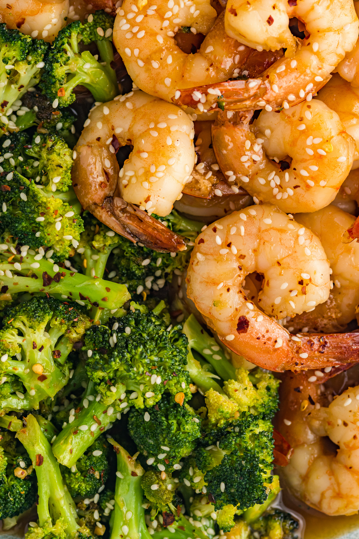 Closeup of cooked shrimp and broccoli that has been garnished with white sesame seeds and red pepper flakes.