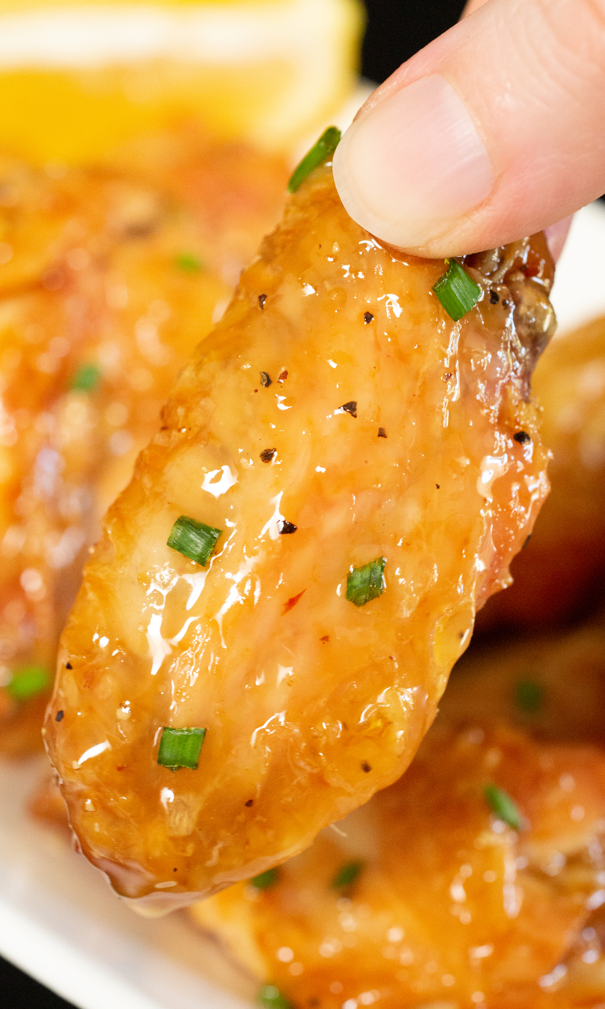 Close up of a Honey Lemon Pepper Wing held up over the basket of them.