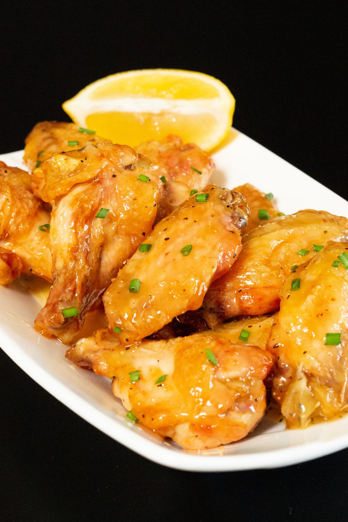 Glazed honey lemon pepper wings on a black background.