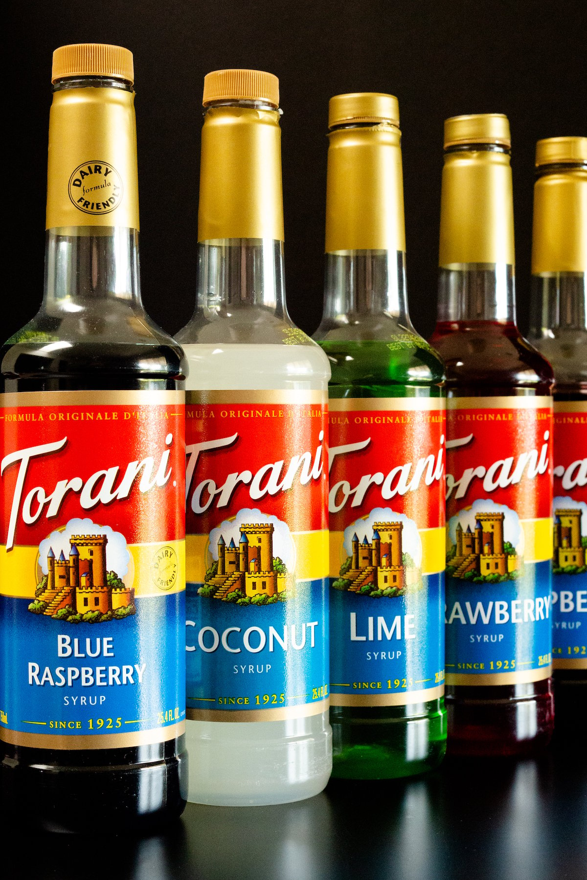 Five different bottles of flavored Torani syrup on a black background.