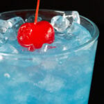 Close up of a glass of ocean water with a cherry on top.