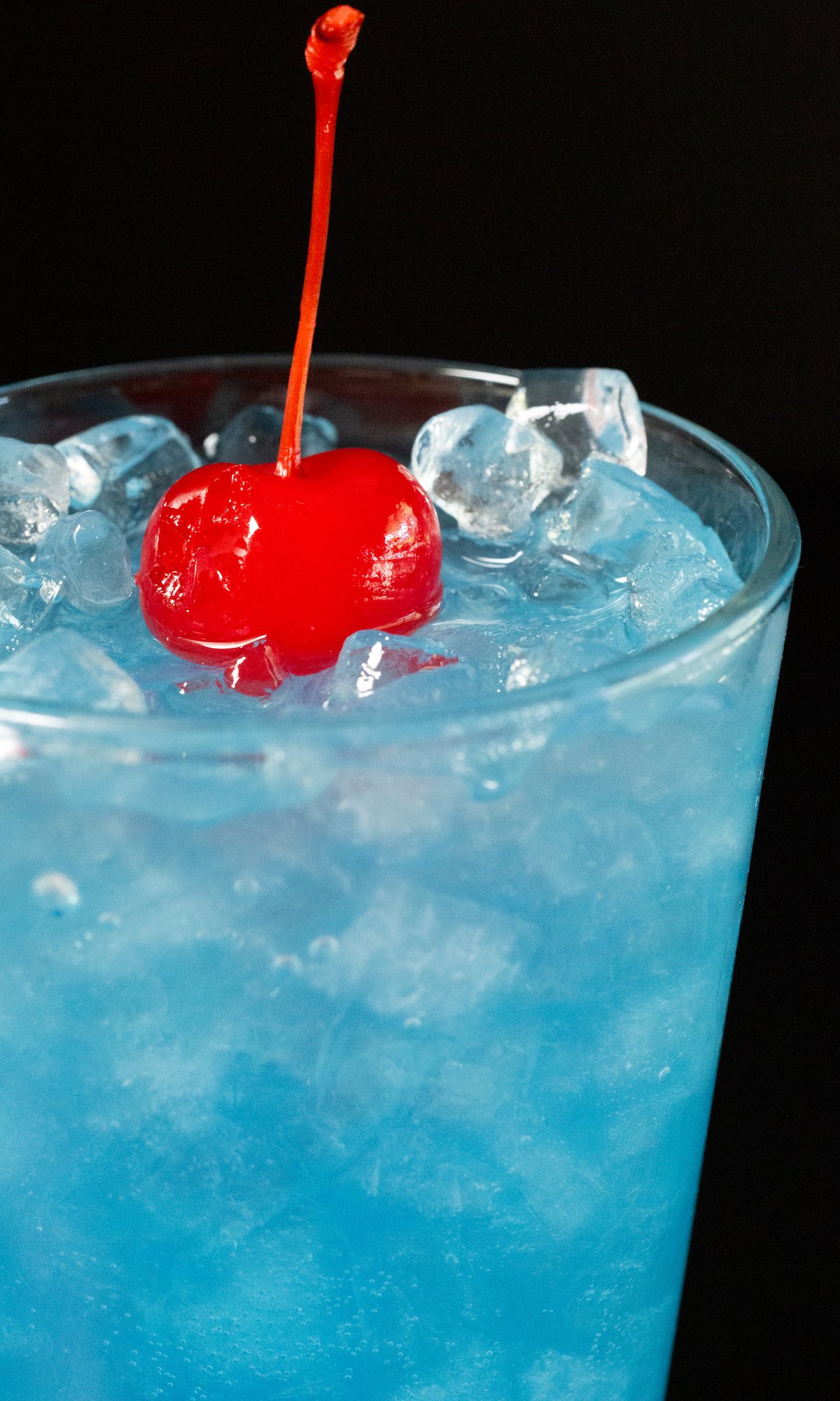 Close up of a glass of ocean water with a cherry on top.
