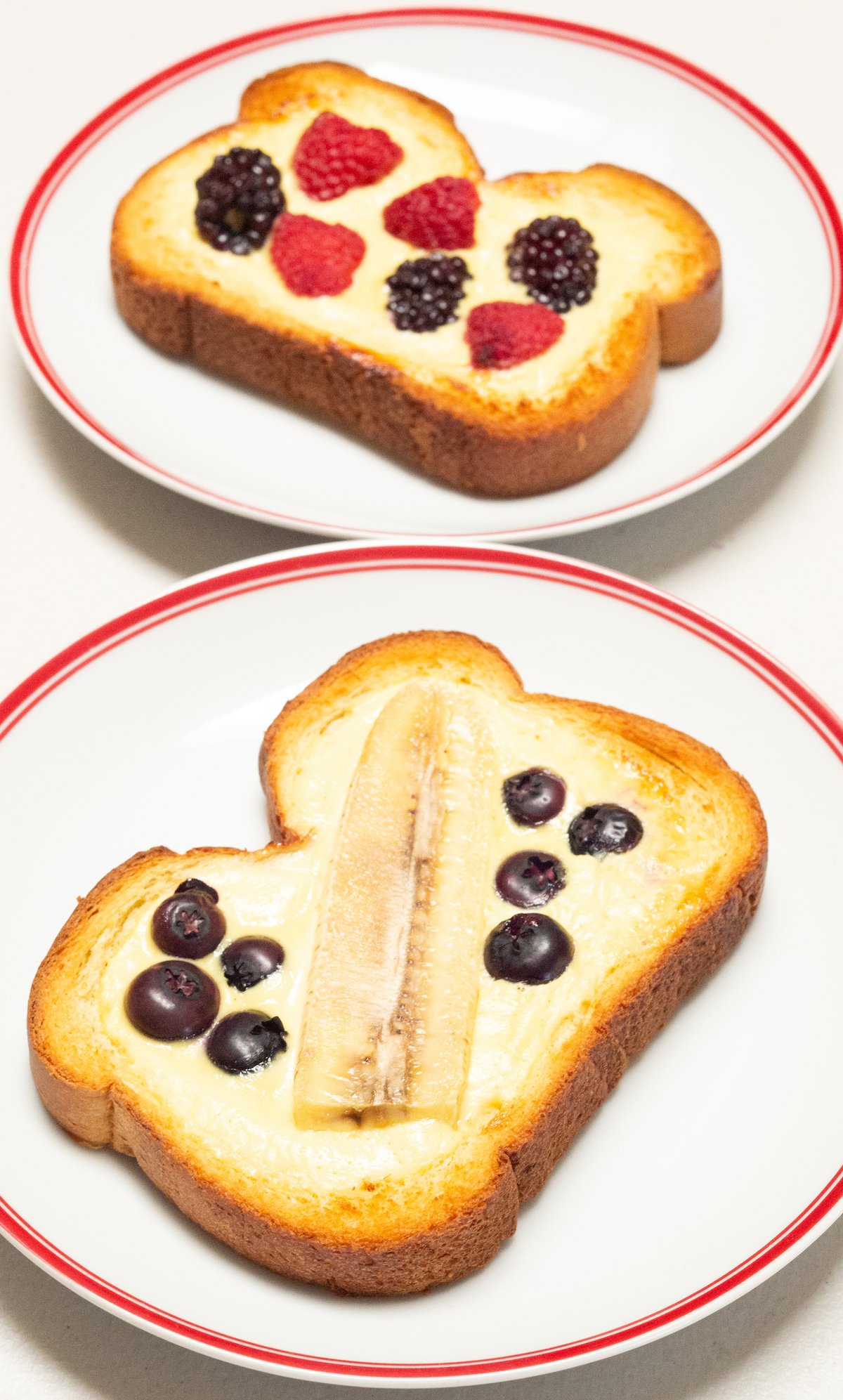 Two dinner plates each with a slice of yogurt custard toast topped with fresh fruit.