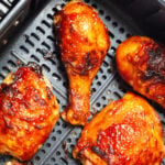 Cooked BBQ chicken legs and thighs in an air fryer basket.