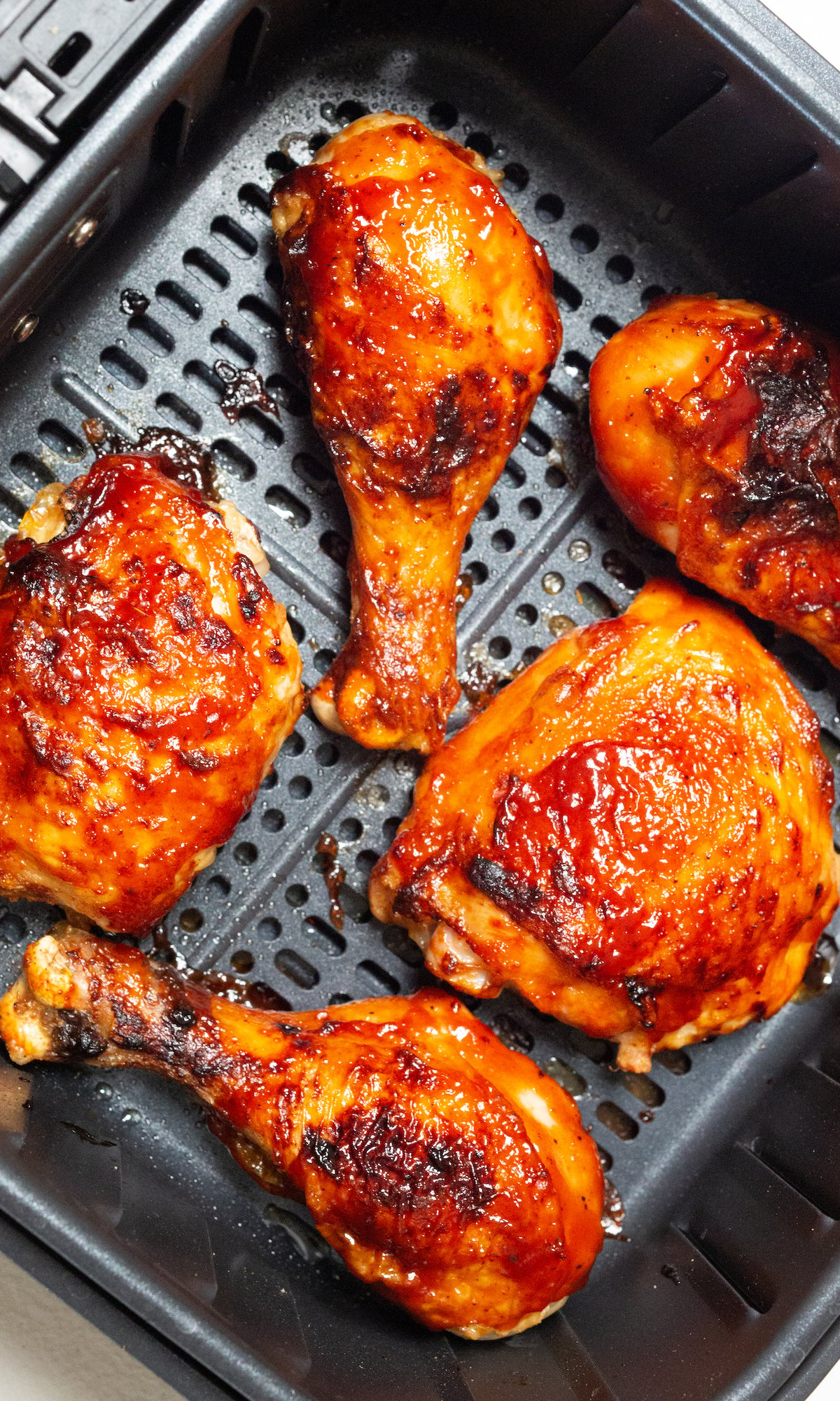 Cooked BBQ chicken legs and thighs in an air fryer basket.