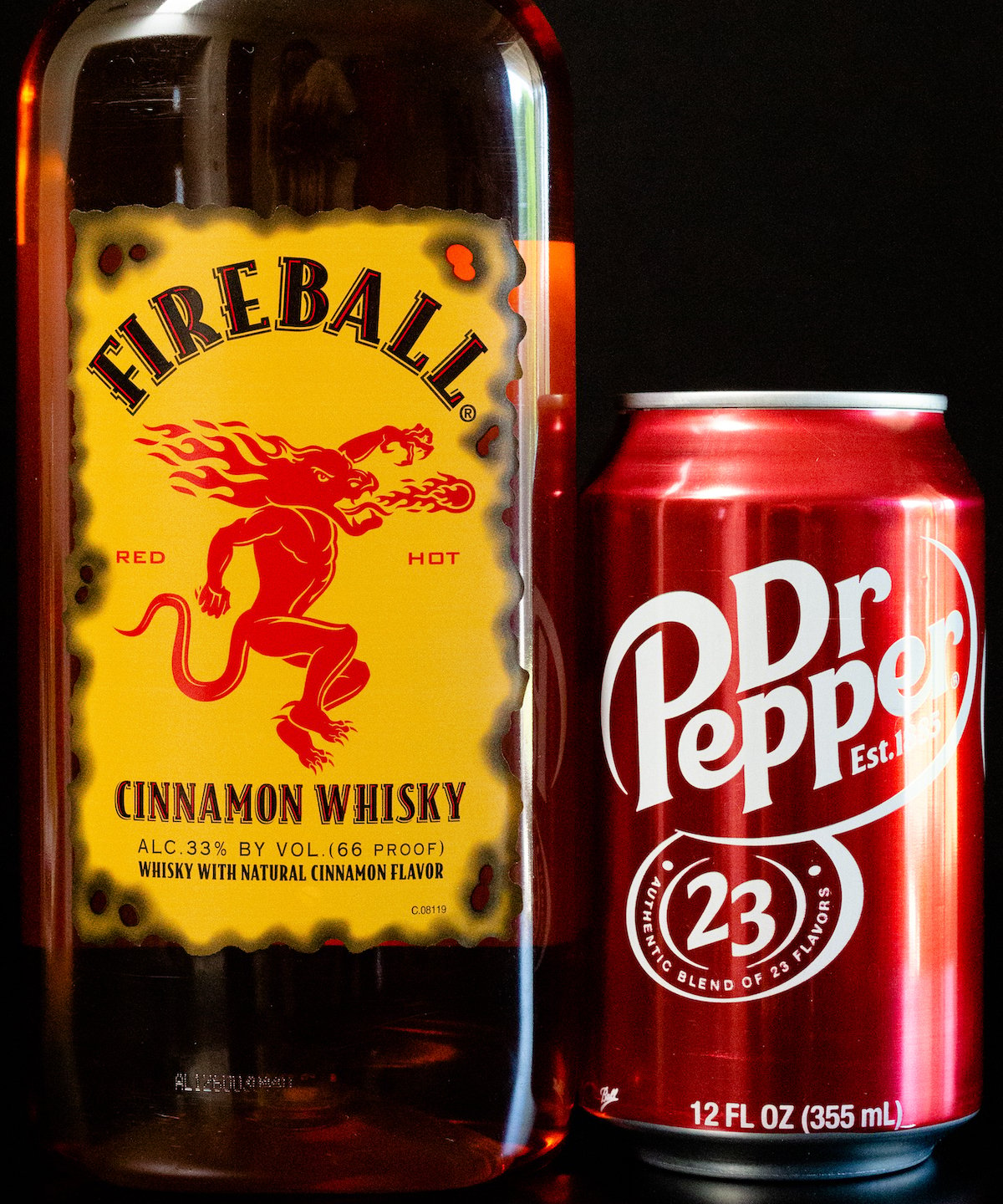 A bottle of Fireball whiskey and a can of Dr. Pepper on a black background.