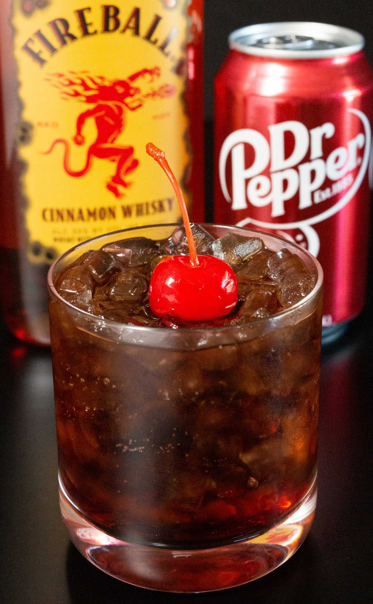 A rocks glass with fireball and dr. pepper sits in front of a bottle of each.