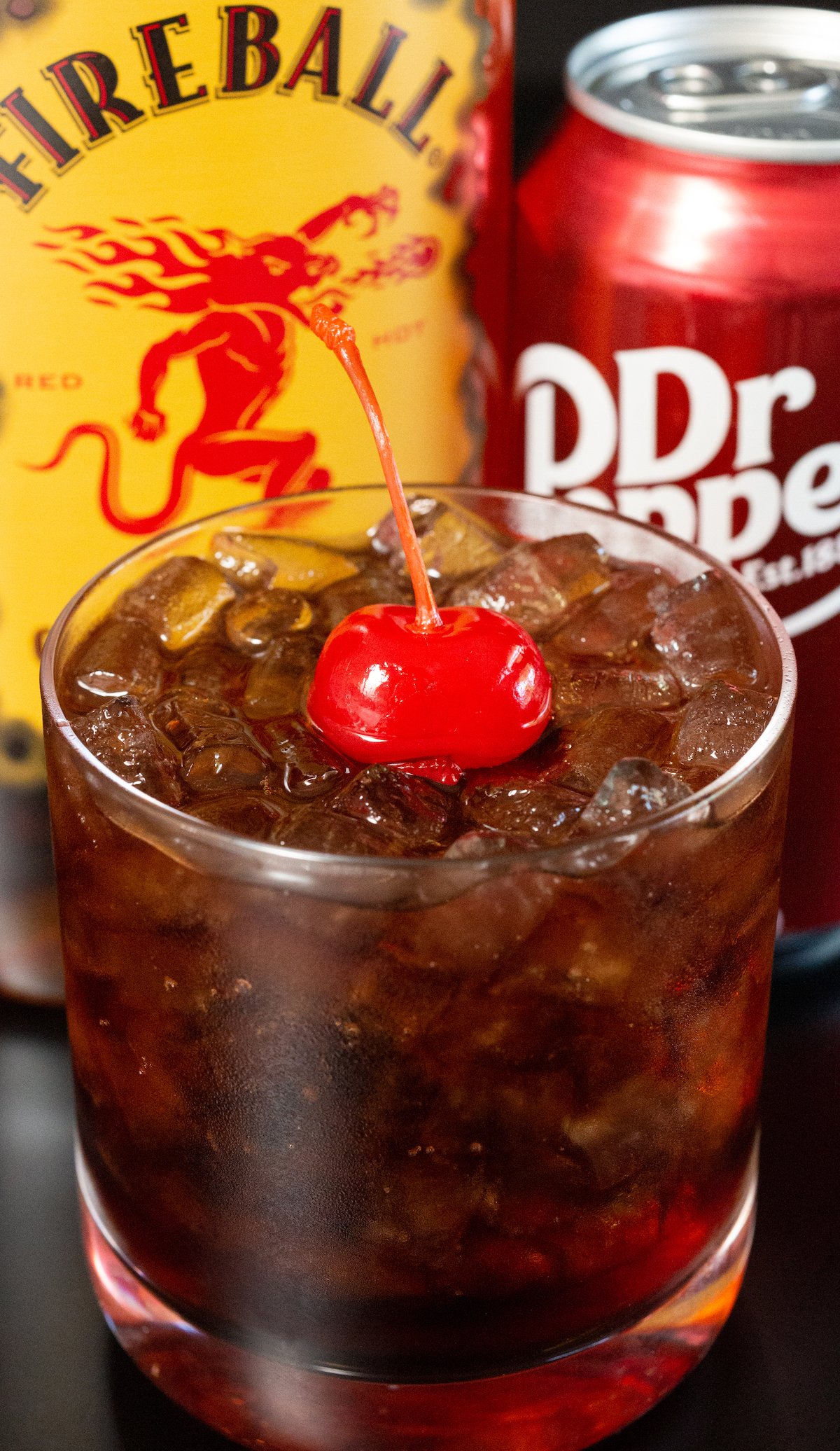 A fireball dr. pepper cocktail in a rocks glass with a cherry on top.