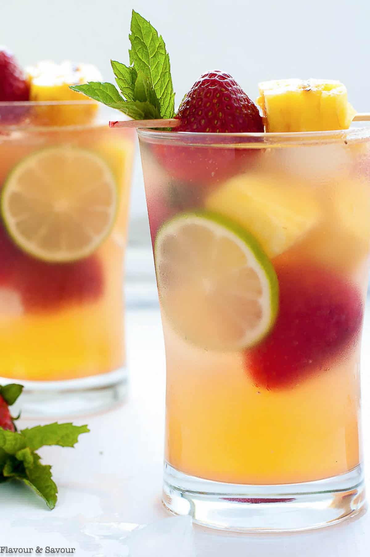 A glass filled with sangria, pineapple chunks, whole strawberries, and lime wheels.