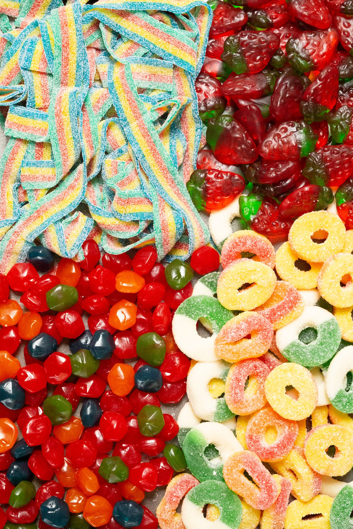 A baking sheet filled with candy - sour rainbow belts, strawberry gummies, Gushers, peach and green apple rings.