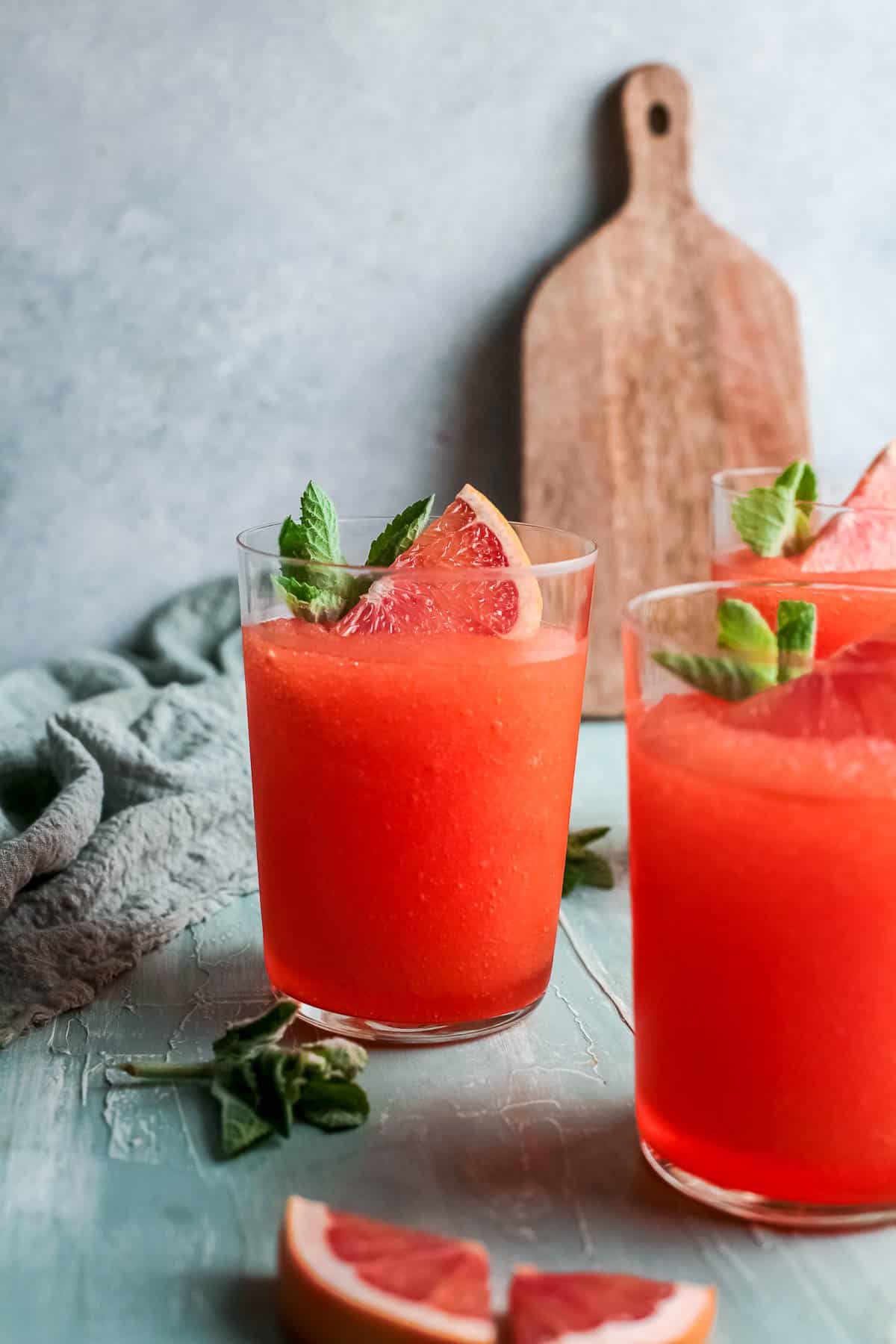 Three glasses of frozen aperol spritz garnished with grapefruit and mint.