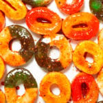 Green apple and peach gummy rings covered in Chamoy and Tajin on parchment paper.